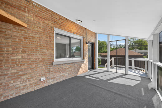 Screened porch with exposed brick wall and door to rear deck at 9205 S Utica Ave