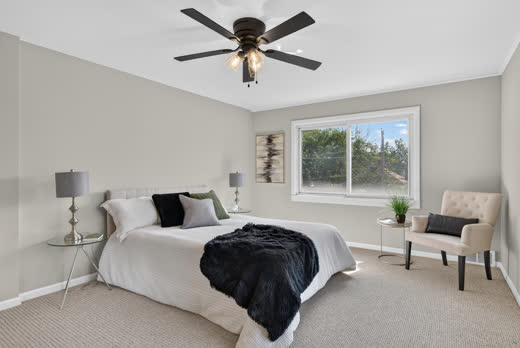 Staged primary bedroom with neutral decor and treetop window views at 9205 S Utica Ave